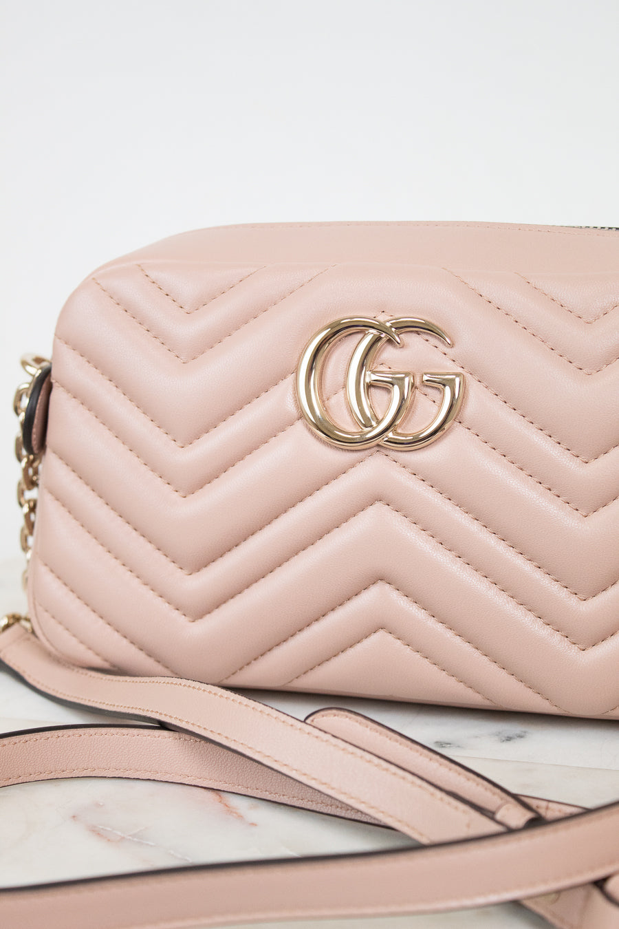A light pink quilted leather shoulder bag with a gold-tone interlocking G logo on the front, resting on a white marble surface with a white background.