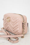 A light pink quilted leather camera bag with gold-tone hardware, featuring a chevron pattern, a gold interlocking G logo, and a matching shoulder strap on a white marble surface.