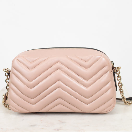 A light pink quilted leather handbag with a chevron pattern and a gold chain strap, resting on a white marble surface against a white background.