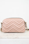 A light pink quilted leather handbag with a chevron pattern and a gold chain strap, resting on a white marble surface against a white background.