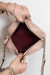 A light pink quilted leather handbag with gold-tone hardware, shown open with a burgundy interior. A person's hands with bracelets are holding the bag open against a plain white background.