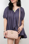 A woman wearing a dark purple short-sleeve button-up dress and holding a light pink quilted shoulder bag with a gold interlocking G logo, shown against a plain light gray background.