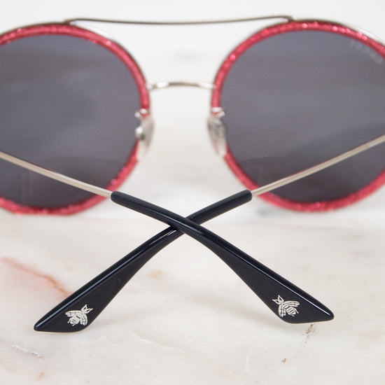 Round sunglasses with red frames and black lenses on a light background