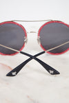 Round sunglasses with red frames and black lenses on a light background