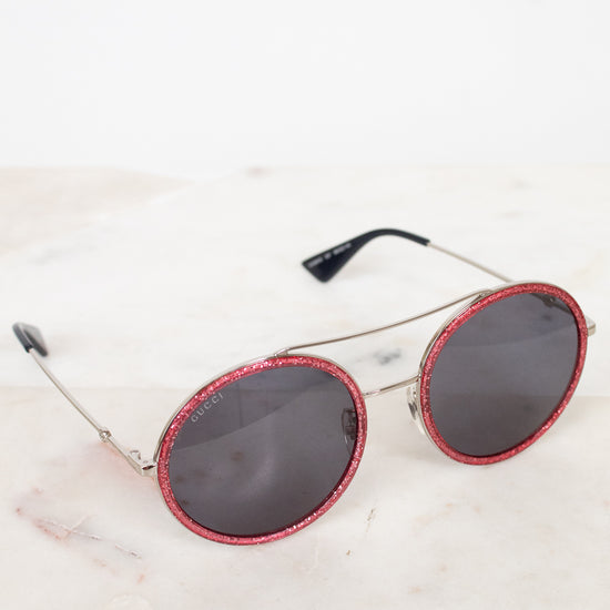 Round sunglasses with red frames and dark lenses on a light marble surface