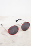 Round sunglasses with red frames and dark lenses on a light marble surface