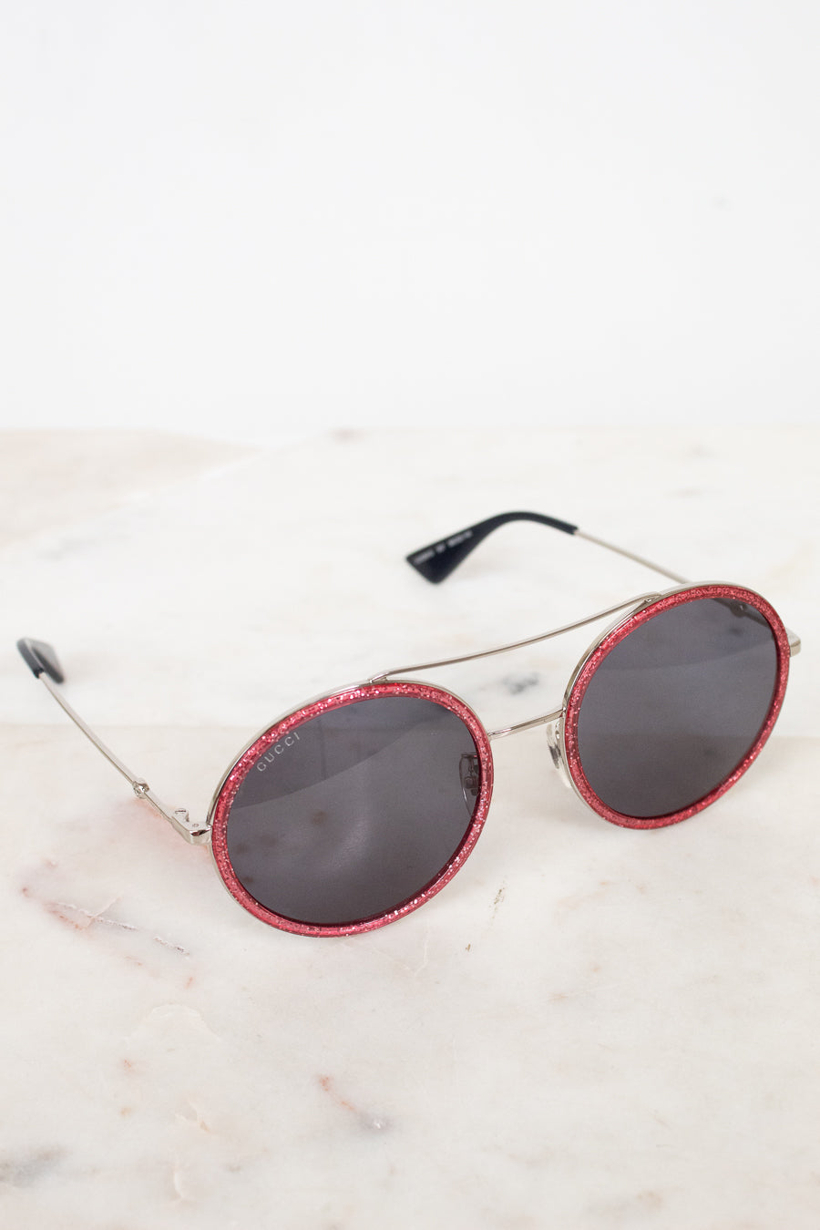 Round sunglasses with red frames and dark lenses on a light marble surface