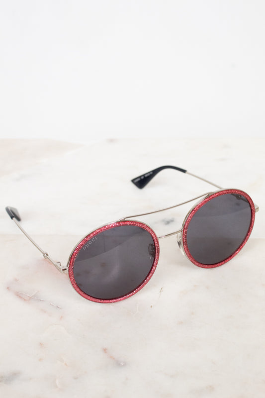 Round sunglasses with red frames and dark lenses on a light marble surface