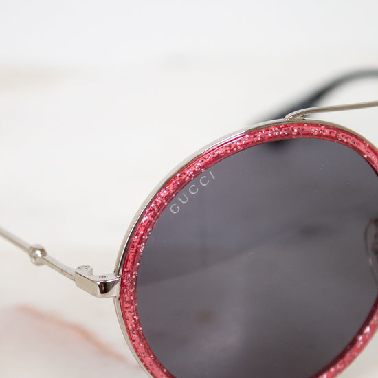 Sunglasses with red glitter frame and Gucci logo on a light background