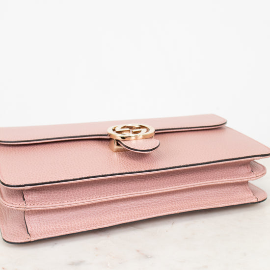 Pink handbag with gold logo detail on a white marble surface