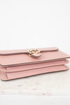 Pink handbag with gold logo detail on a white marble surface