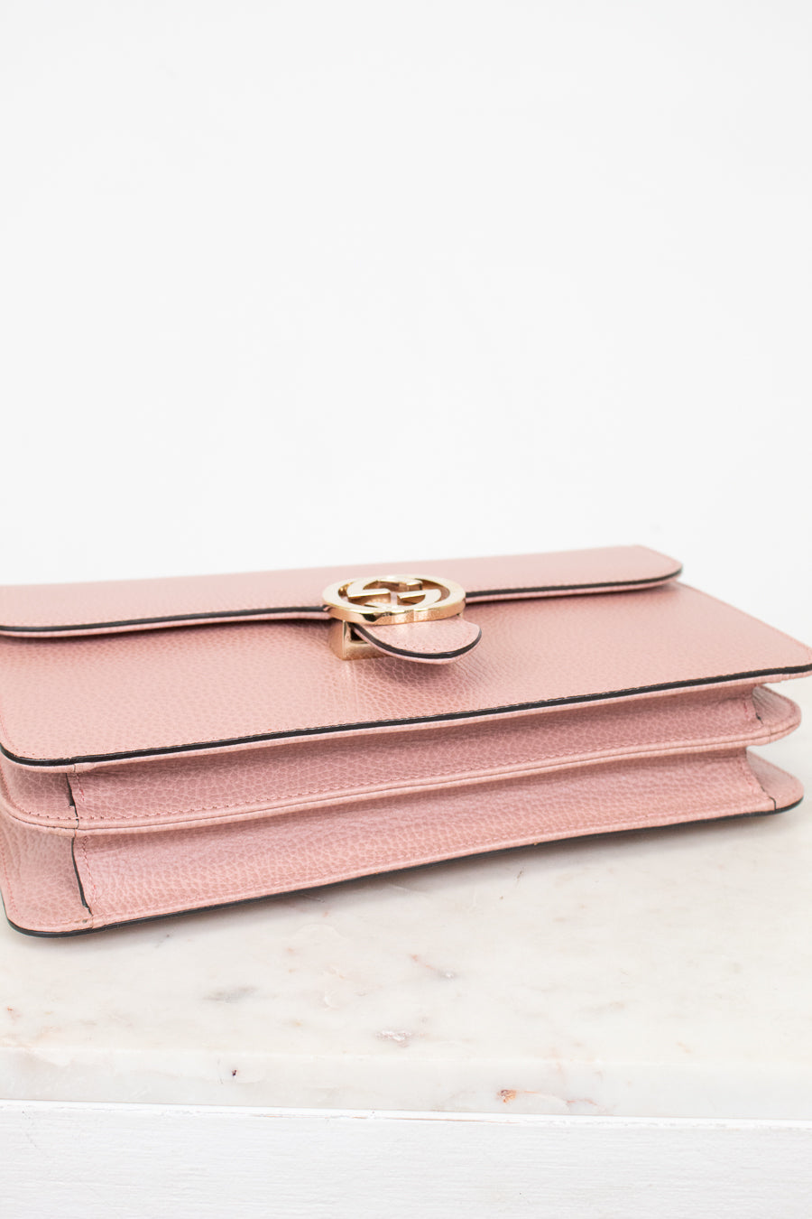 Pink handbag with gold logo detail on a white marble surface