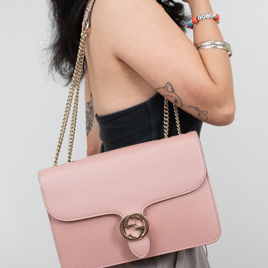 Person holding a pink handbag with a gold chain strap against a plain background
