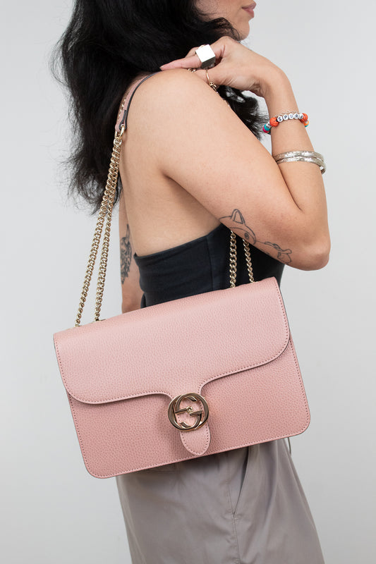 Person holding a pink handbag with a gold chain strap against a plain background