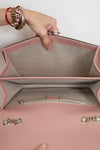 Pink handbag with gold accents held open by a hand, showing the interior.
