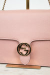 Pink handbag with a gold logo on a marble surface