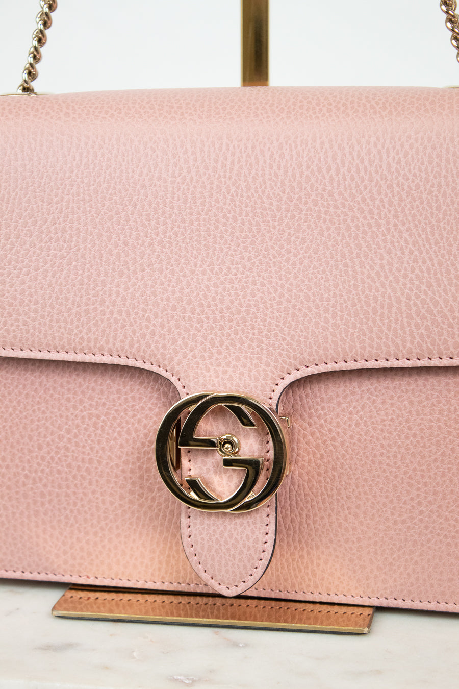 Pink handbag with a gold logo on a marble surface