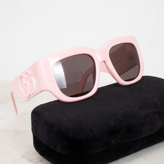Pink sunglasses with dark lenses on a black case against a light background