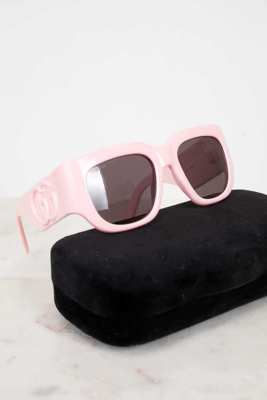 Pink sunglasses with dark lenses on a black case against a light background