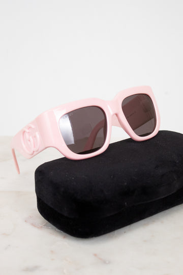 Pink sunglasses with dark lenses on a black case against a light background