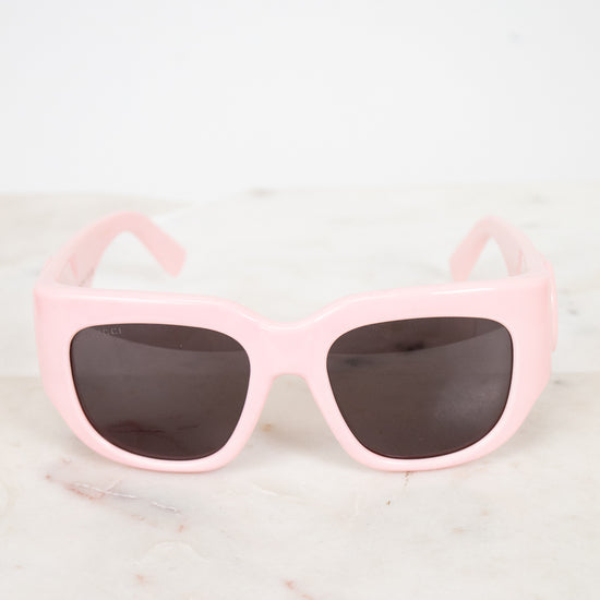 Pink sunglasses with dark lenses on a light marble background