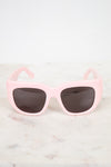Pink sunglasses with dark lenses on a light marble background
