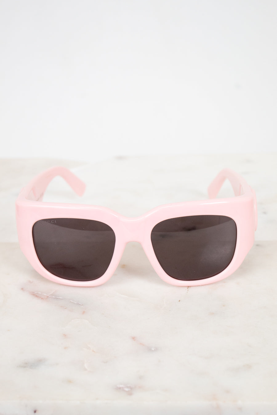 Pink sunglasses with dark lenses on a light marble background