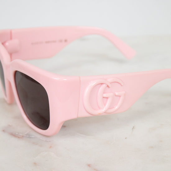 Pink sunglasses with a brand logo on a marble surface