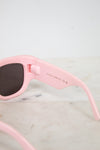 Pink sunglasses with dark lenses on a light marble surface