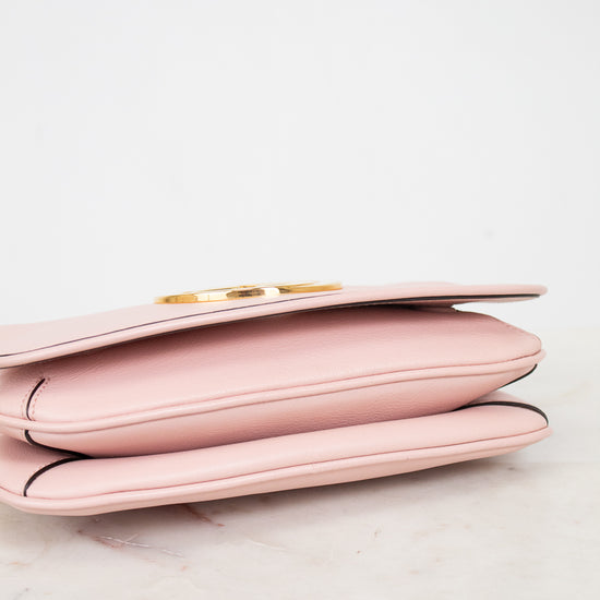 Bottom view of a light pink leather purse with a gold-tone metal clasp, resting on a white marble surface against a white background.