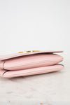 Bottom view of a light pink leather purse with a gold-tone metal clasp, resting on a white marble surface against a white background.