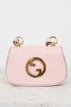 A light pink leather shoulder bag with a gold-tone interlocking G logo on the front and matching gold ring handles, displayed on a light marble surface against a white background.