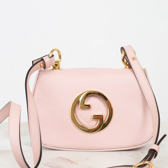 A light pink leather shoulder bag with a prominent gold interlocking G logo on the front, displayed on a light marble surface against a white background.