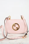 A light pink leather shoulder bag with a prominent gold interlocking G logo on the front, displayed on a light marble surface against a white background.