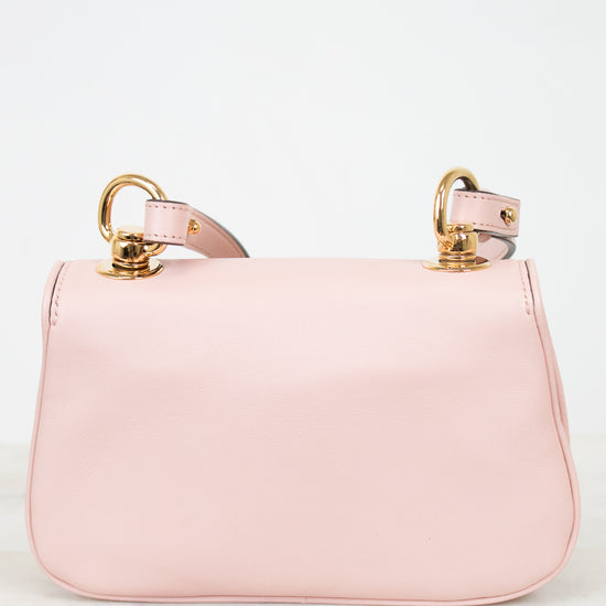 A light pink leather shoulder bag with gold-tone hardware and a matching pink strap, displayed on a light marble surface against a white background.