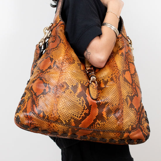 Person holding a large brown snake skin patterned handbag against a white background