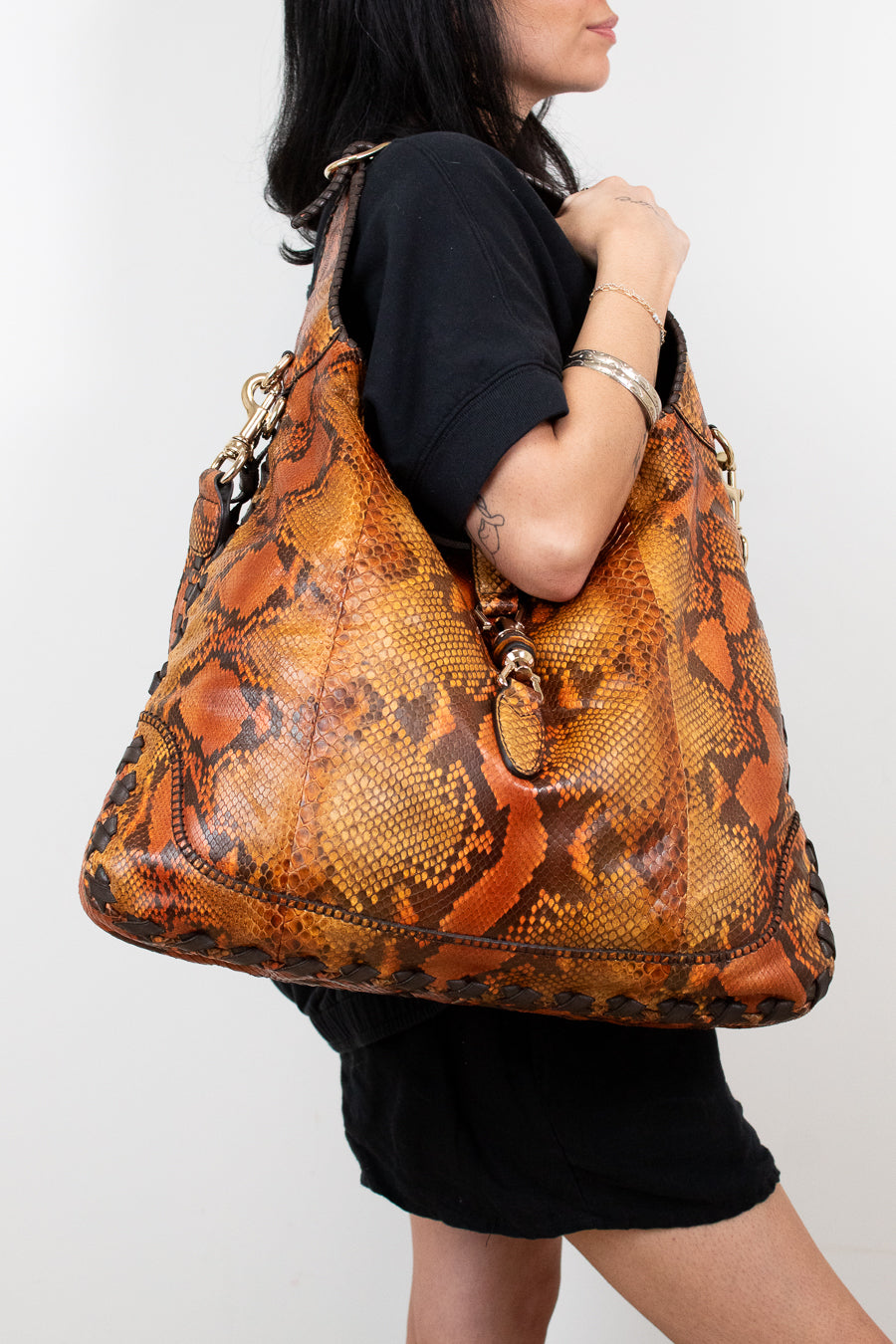 Person holding a large brown snake skin patterned handbag against a white background