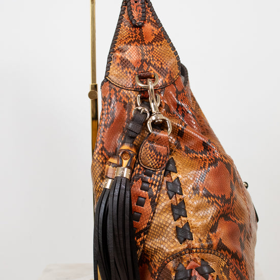 Brown leather sling bag with snake skin pattern on a white background