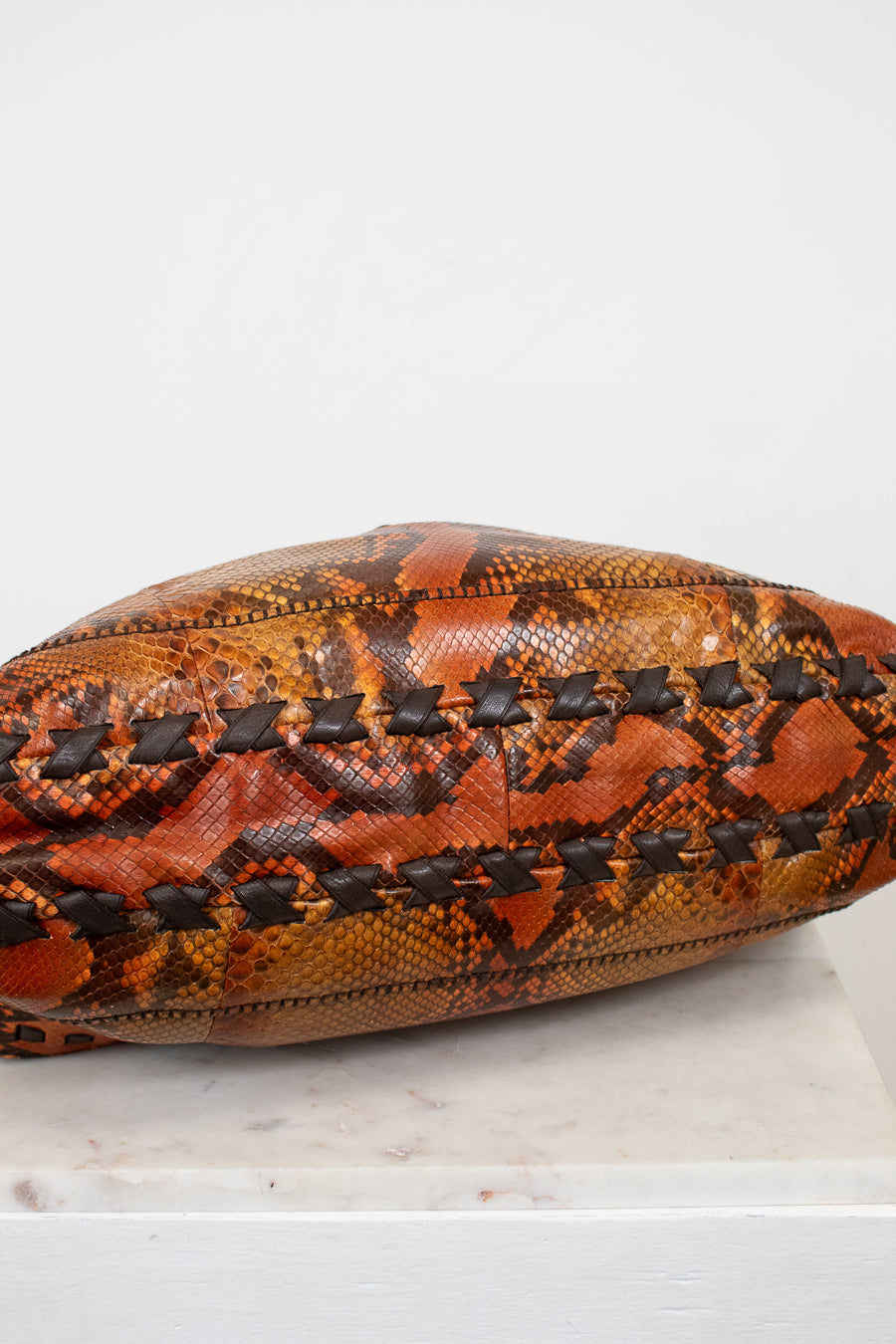 Snakeskin-patterned bag with black stitching on a white background