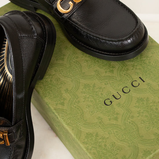 Black Gucci loafers with gold logo on a green Gucci box.