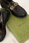 Black Gucci loafers with gold logo on a green Gucci box.
