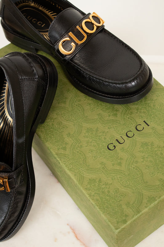 Black Gucci loafers with gold logo on a green Gucci box.