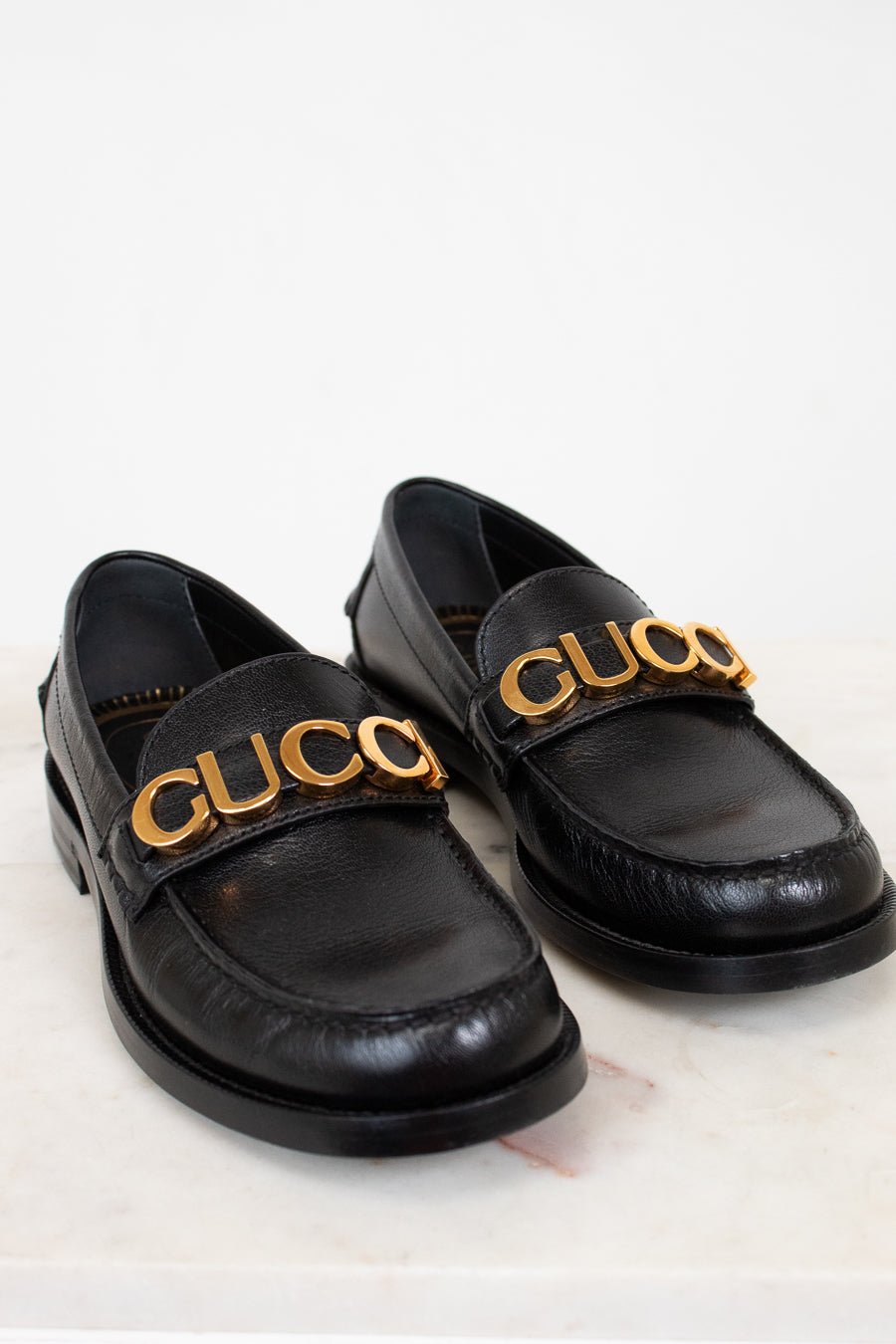 Black loafers with gold 'Gucci' logo on a light background