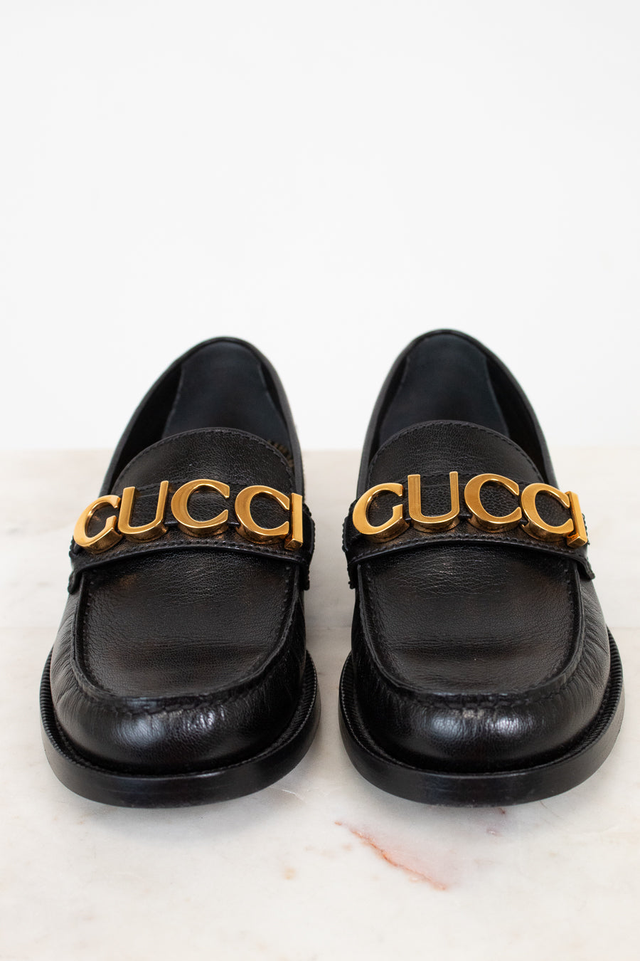 Pair of black loafers with gold 'Gucci' logo on a white background