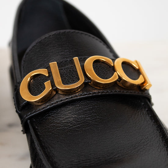 Black loafer with gold 'Gucci' logo on a light background