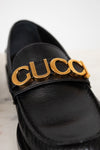 Black loafer with gold 'Gucci' logo on a light background