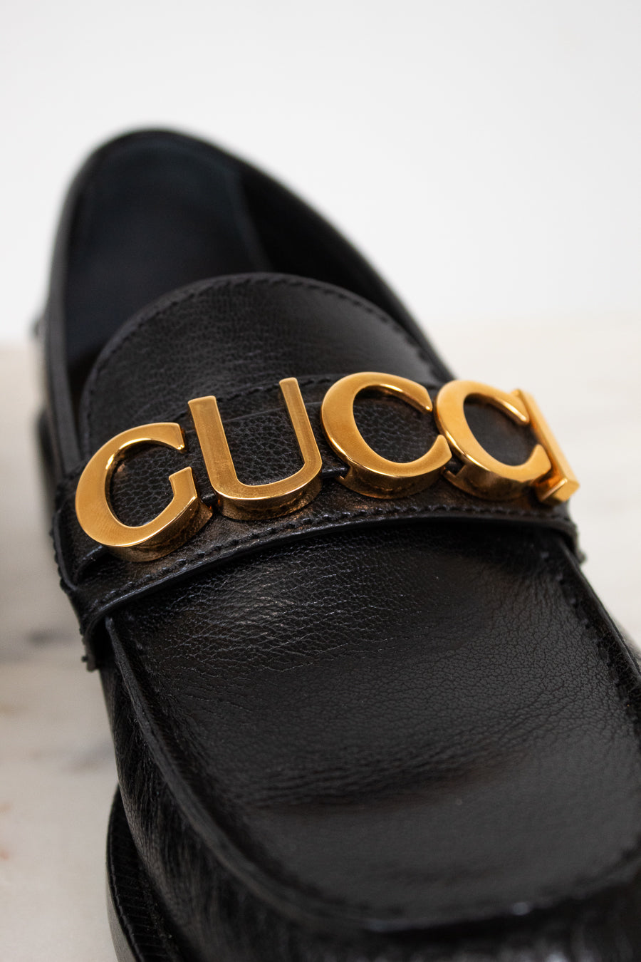 Black loafer with gold 'Gucci' logo on a light background
