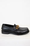 Black loafer shoe with gold logo on a white background