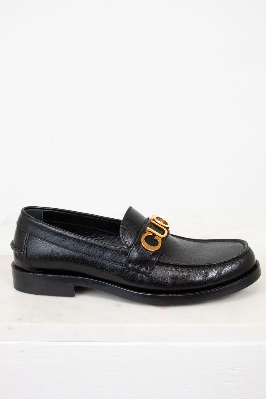 Black loafer shoe with gold logo on a white background