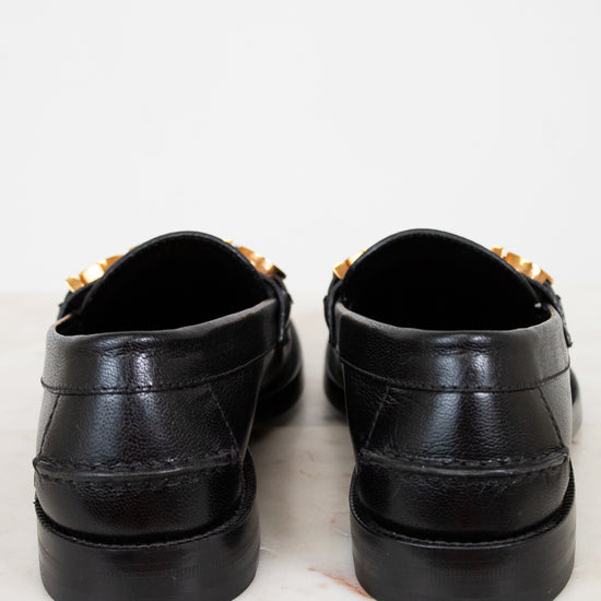 Pair of black loafers with gold accents on a white background